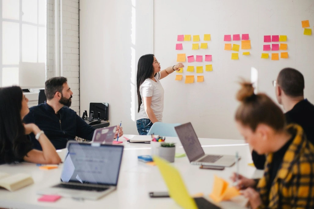 Image of meeting room with woman reading from some post-it notes on a board